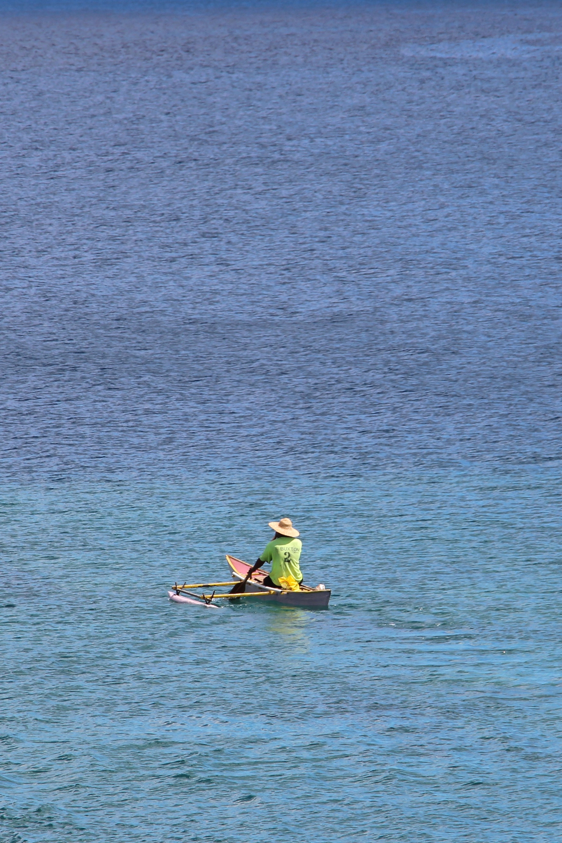 A fisherman in an outrigger canoe on turquoise water